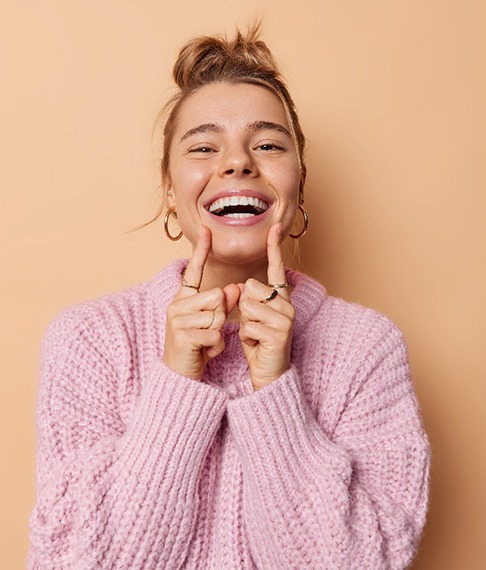 Woman with pink sweater smiling touching corners of her mouth with her pointer fingers