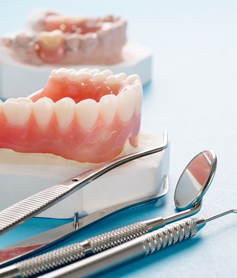 Model of denture next to dental tools