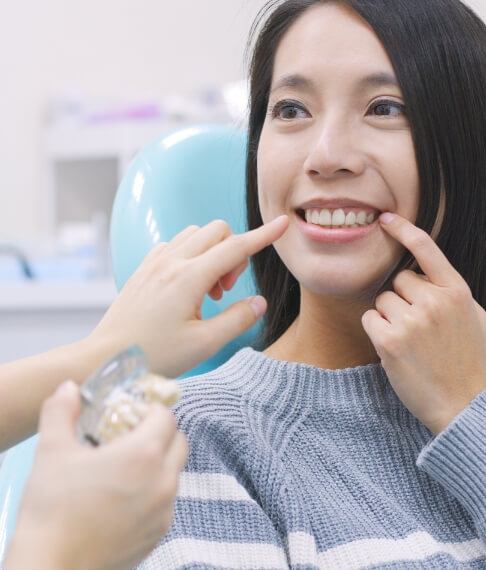 Woman pointing to her smile after tooth replacement with dental implants