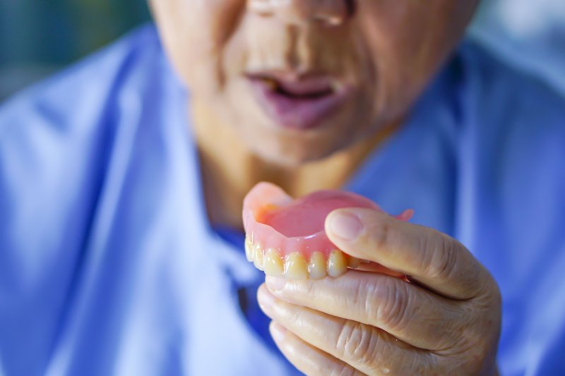 older man holding a full upper denture 
